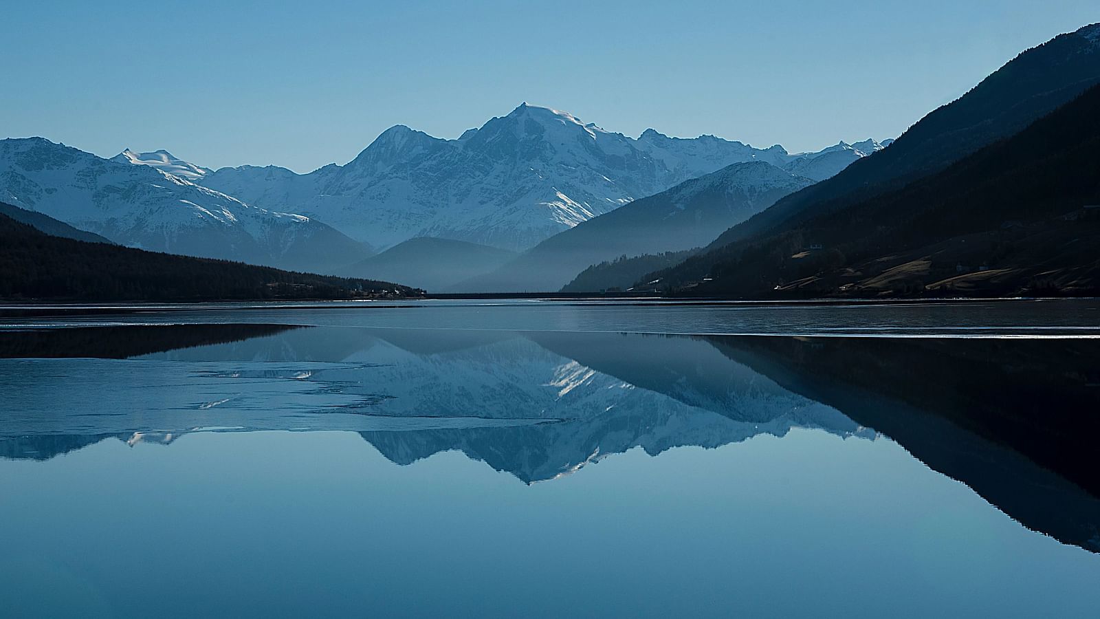 Calm lake reflects mountains, a serene scene under a clear sky.