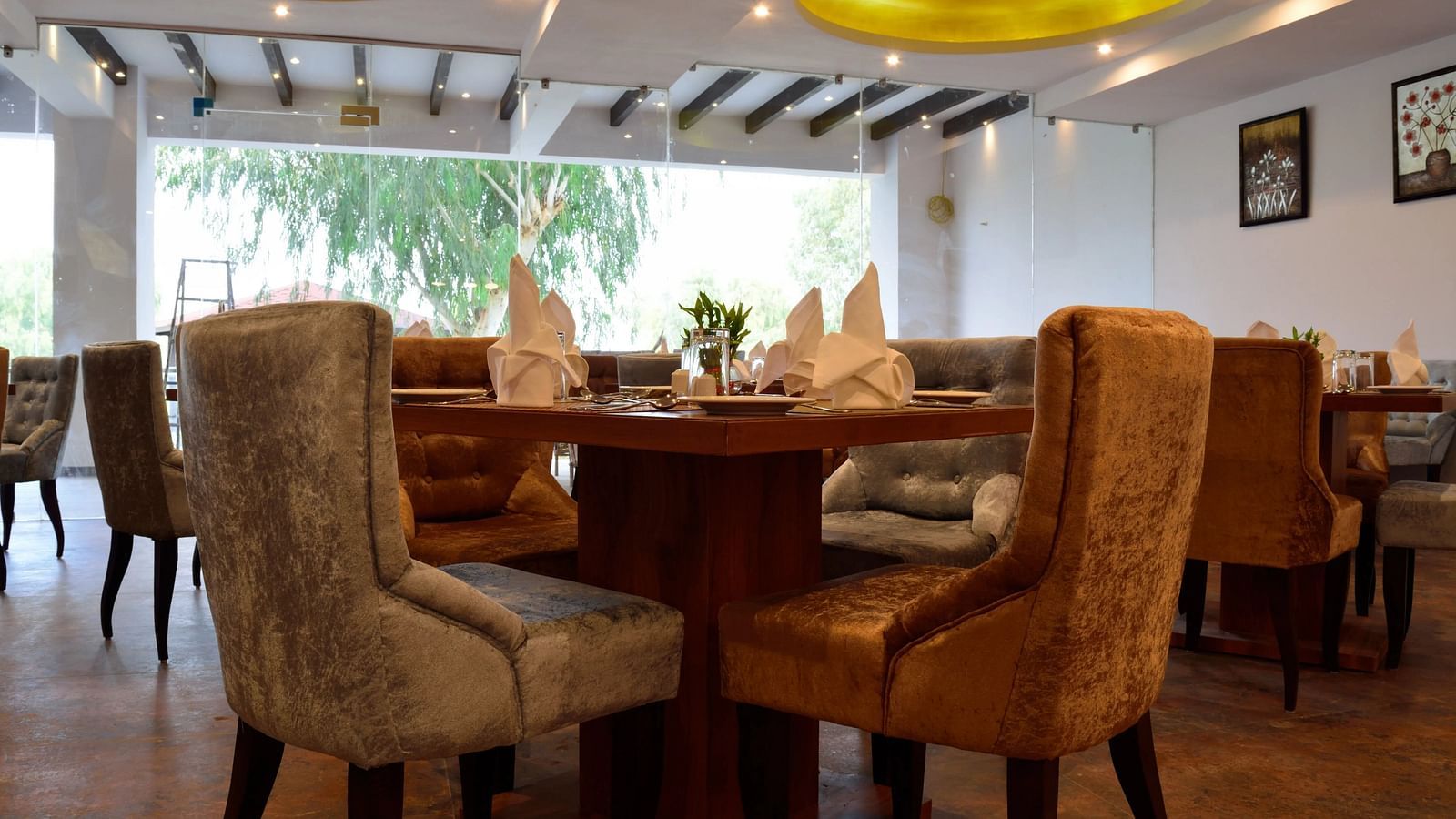Cosy restaurant interior with plush chairs around a wooden table, set with napkins. - Bamboo Saa, Udaipur