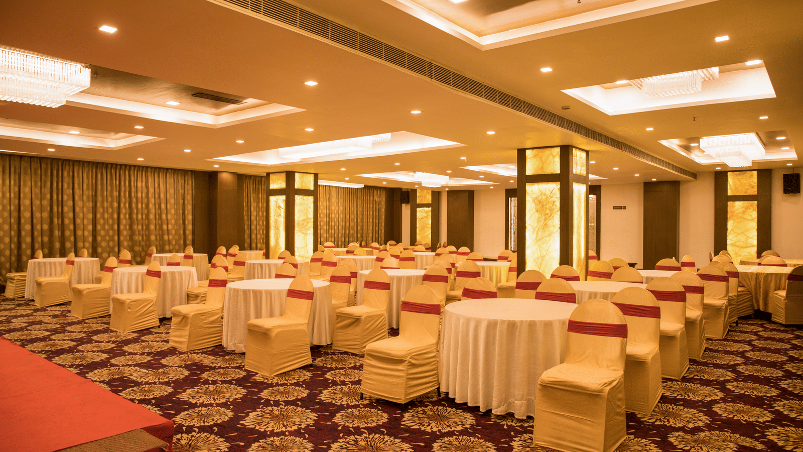 A spacious banquet hall at Benzz Park Chennai with numerous round tables draped in white, set for a gathering.