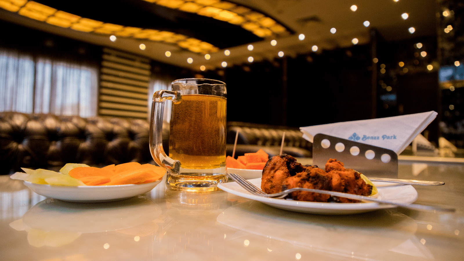 A close up shot of delicious side dish served with a plate of salad and a pint of beer on a dining table at Benzz Park, Vellore.