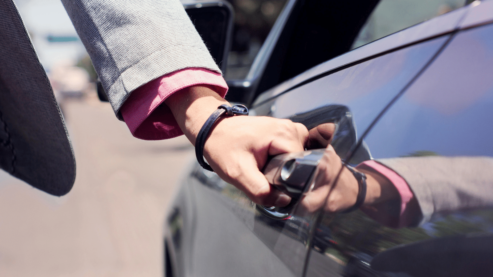A person dressed in business formals opening the door of a car.
