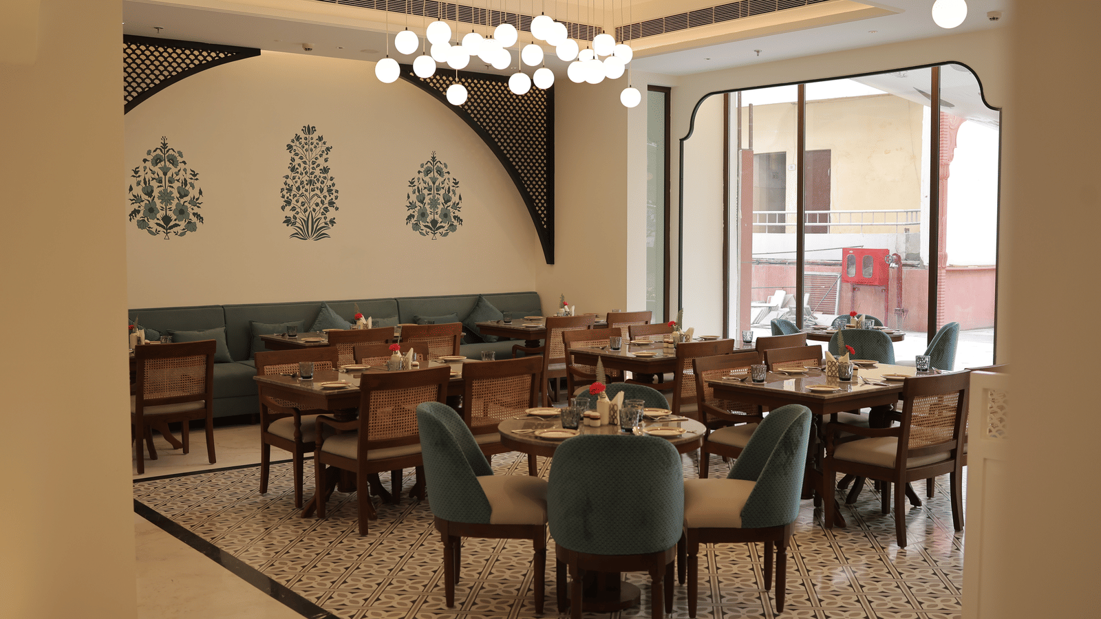 Seating arrangements at the restaurant of Bhagirathi by Atishay under warm lighting featuring chairs and tables by a large ceiling-to-floor window 