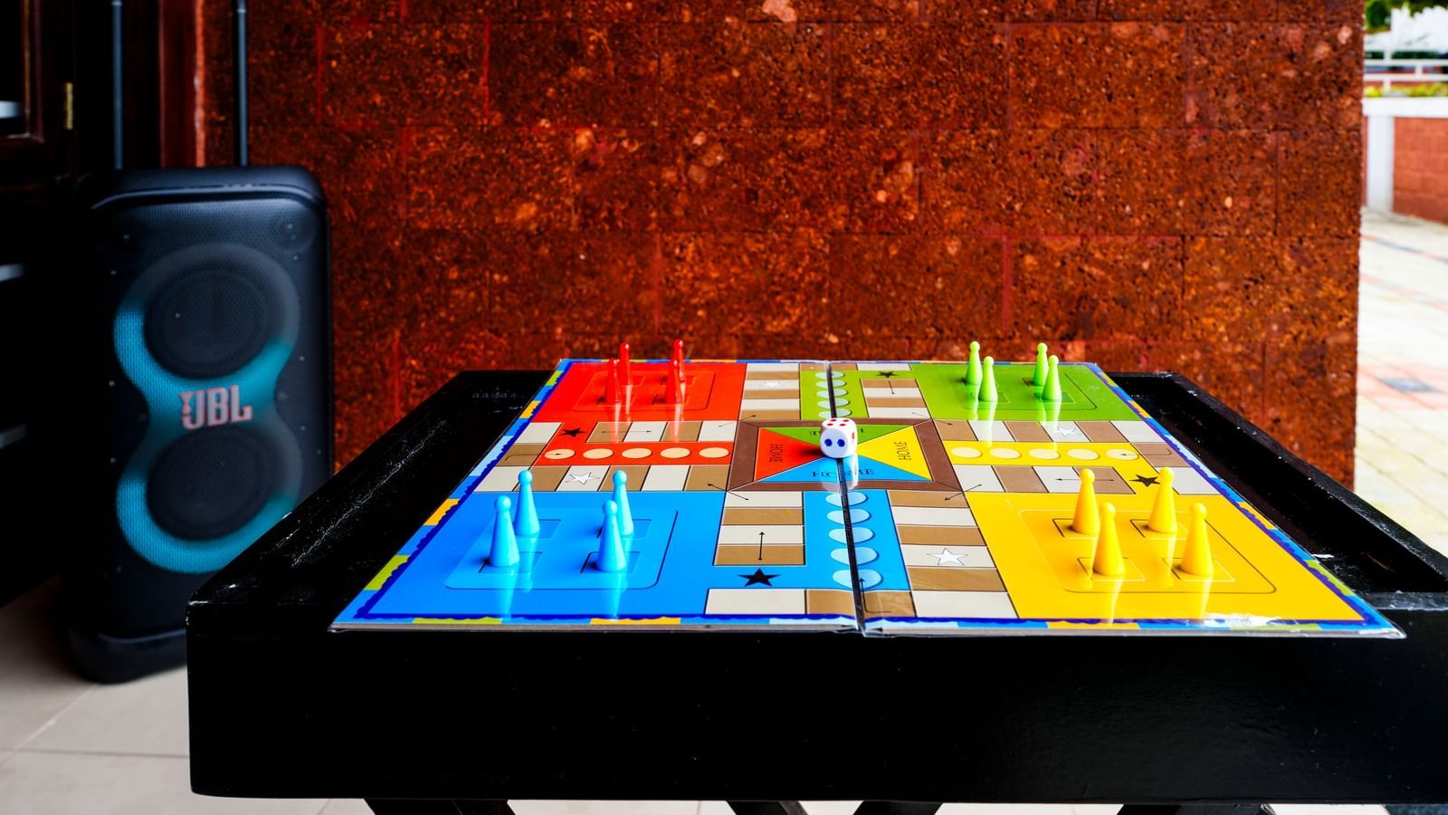 An engaging, close-up shot of a colorful Ludo game board and a large JBL speaker, both set up on a table for indoor entertainment at the retreat.