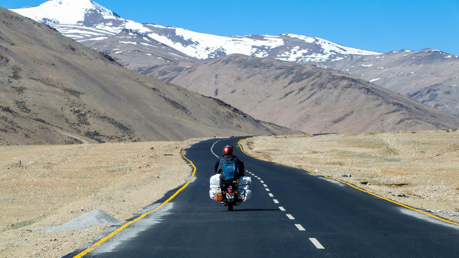 A traveller riding a bike on a remote highway surrounded by mountains