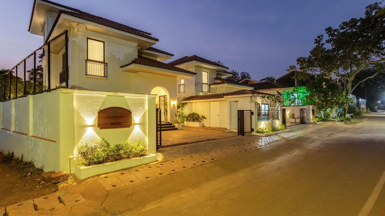 A night view of a luxury villa with warm lighting, a spacious driveway, and manicured greenery - BluSalzz Villas - Alocassia, Anjuna
