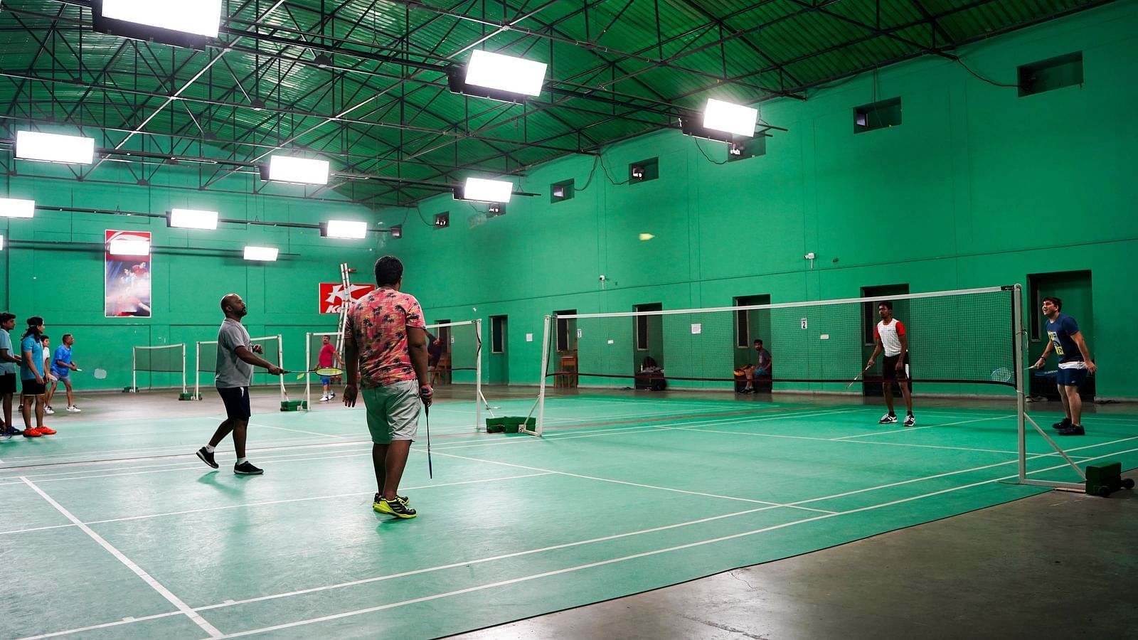 An indoor badminton court with green flooring, showing people playing at BNGV Grandeur Hotel and Banquets.