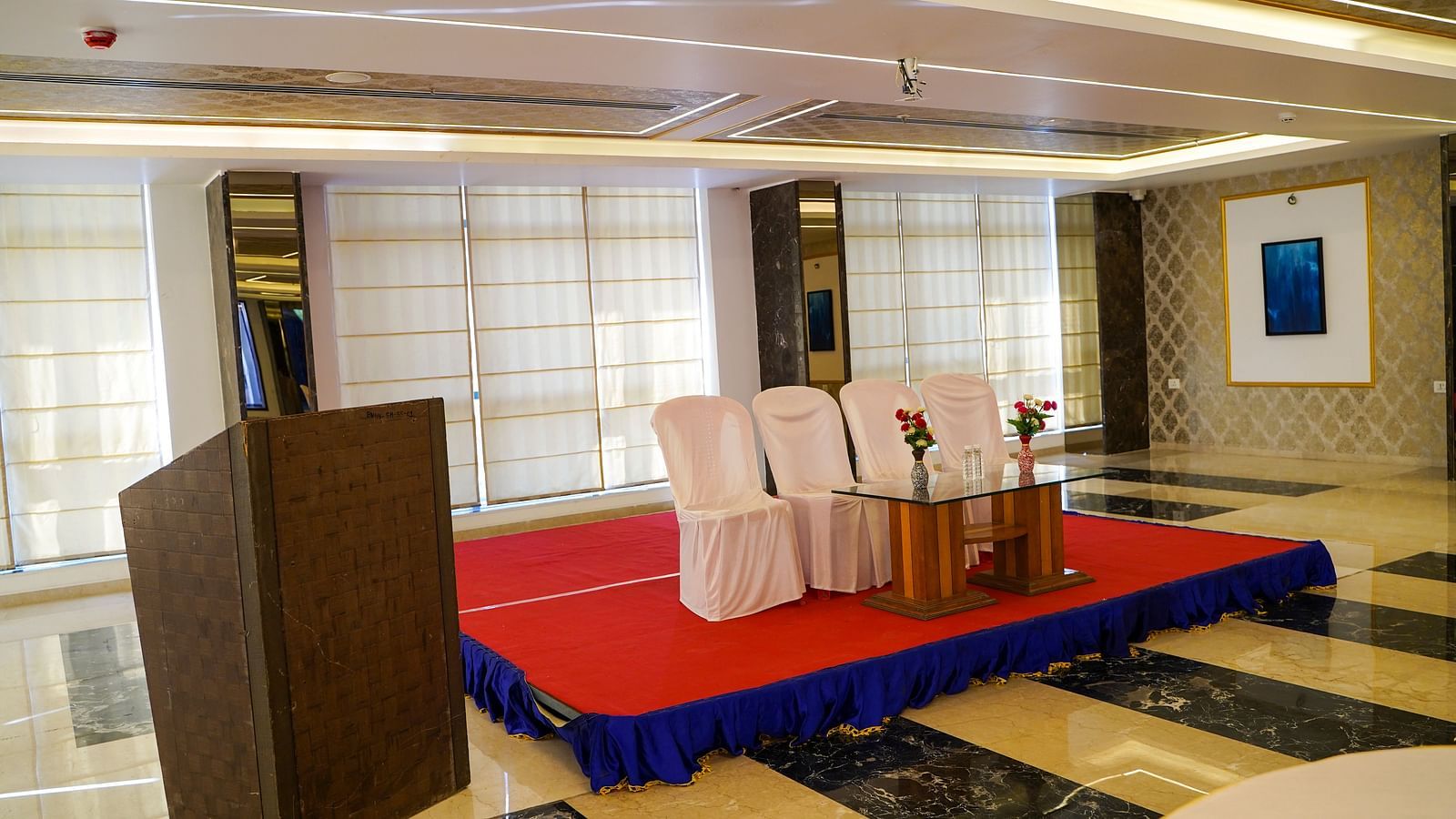 A well-lit smaller space at BNGV Grandeur Hotel and Banquets, arranged for an event with tables, chairs, and a podium.