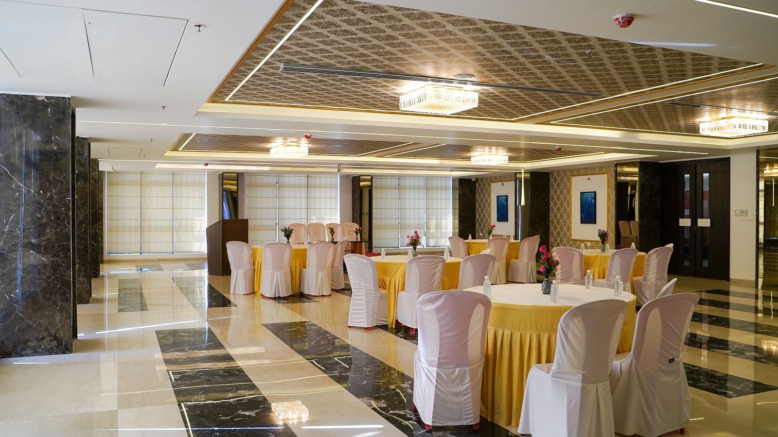 A large, elegant banquet hall with round tables draped in white, and chairs, set up for an event. The floor has a patterned tile design.