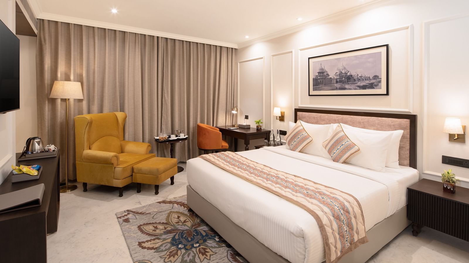 An image of a bedroom with bedside table, photo frame hanged on the wall, work desk with sofa chair, and a flat TV screen - Brij Eternity, Vrindavan