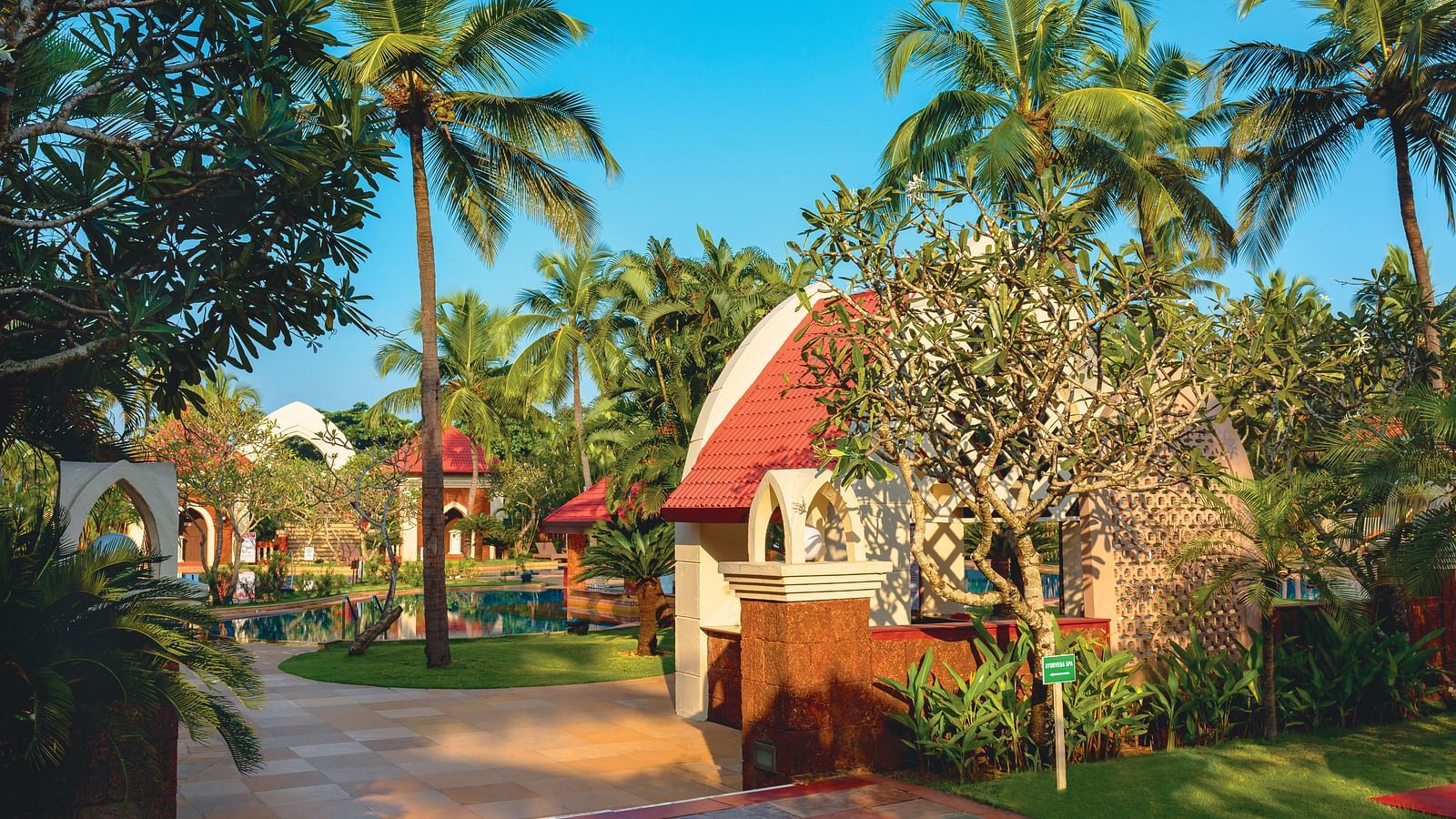 a building surrounded by trees with blue sky in the background - Caravela Beach Resort Goa