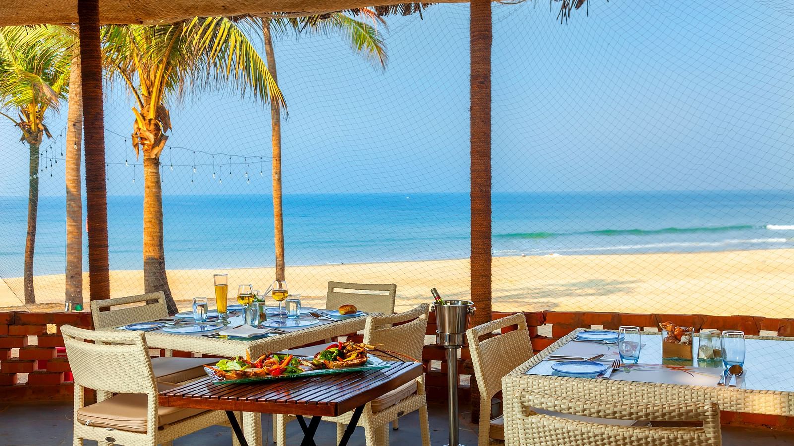 seating arrangements inside the shack with blue sky and beach in view - Caravela Beach Resort Goa.