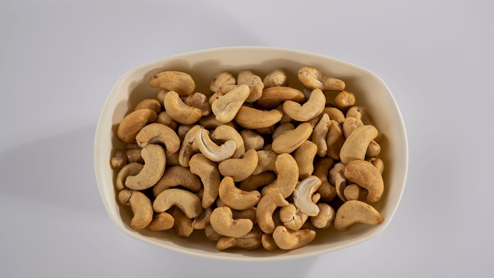 An aerial view of cashews kept in a bowl with the shadow of the bowl seen on the left.