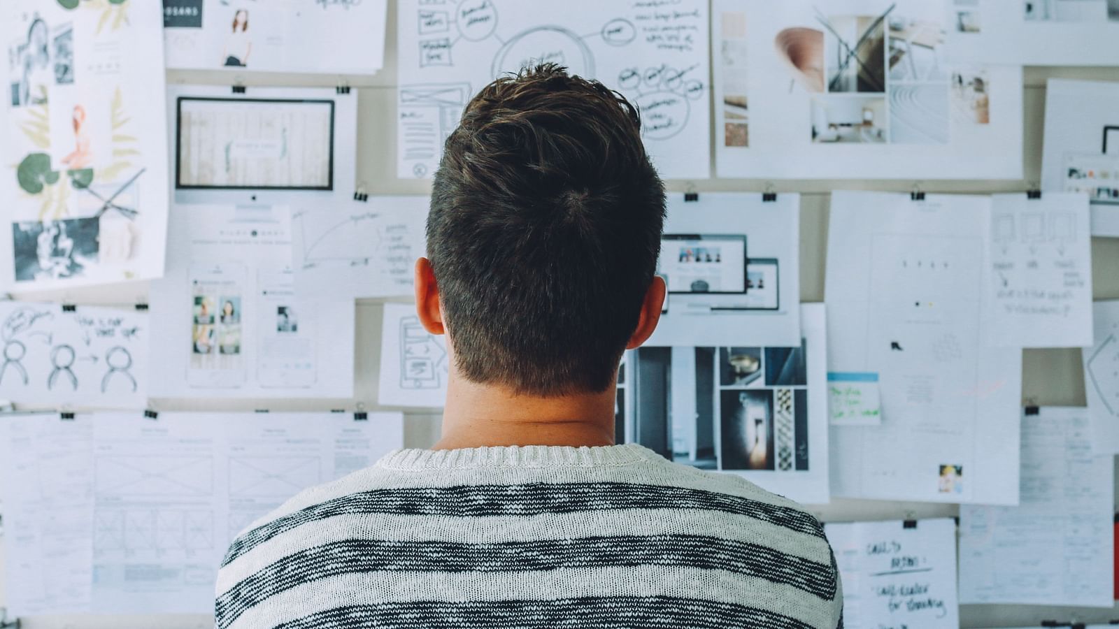 A close up shot of a person looking at the papers stuck on the wall for planning.