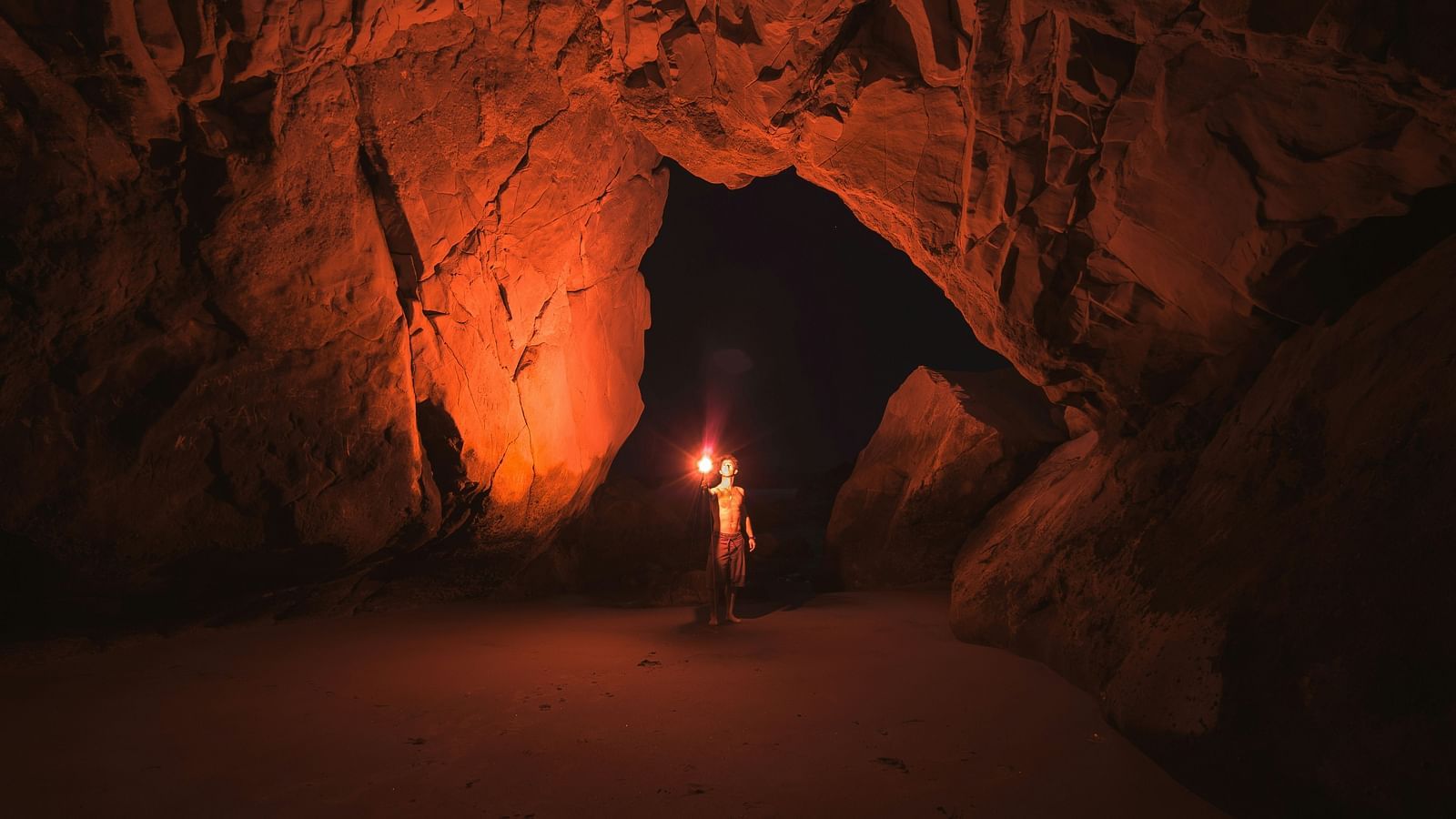 A person holding a stick-fire inside a cave with the light illuminating the area around it
