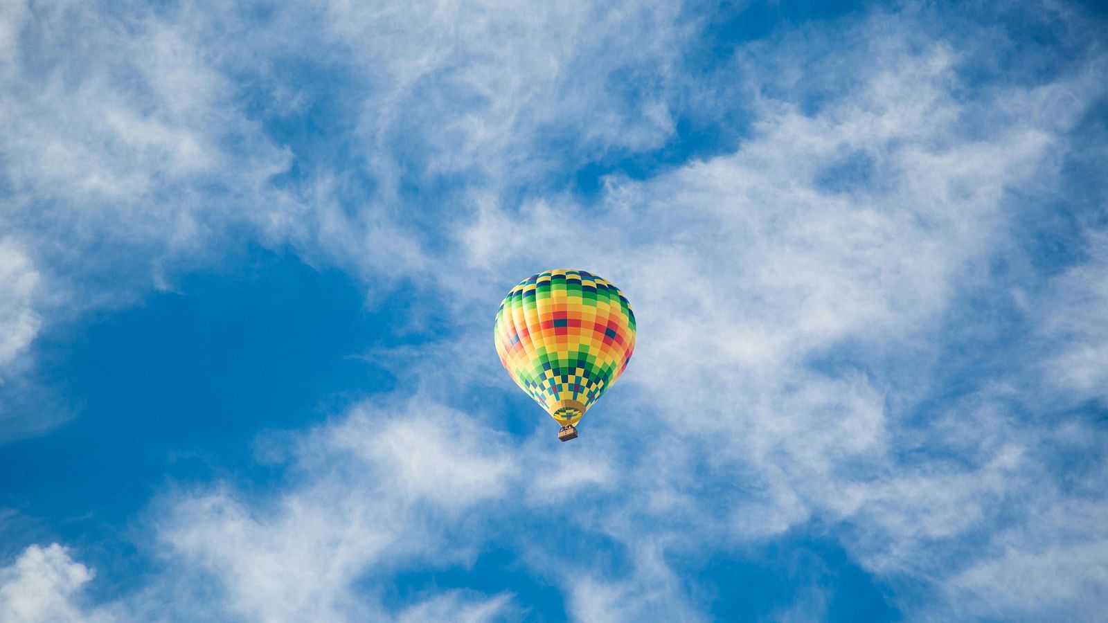 A view from below of a hot air balloon in the sky with white clouds over blue sky in the background