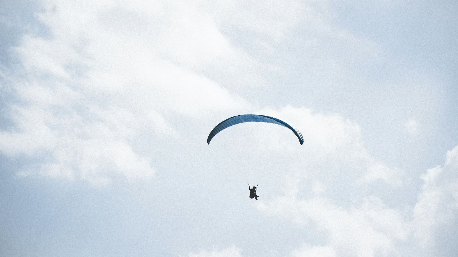 A view from below of a person paragliding with blue sky in the background