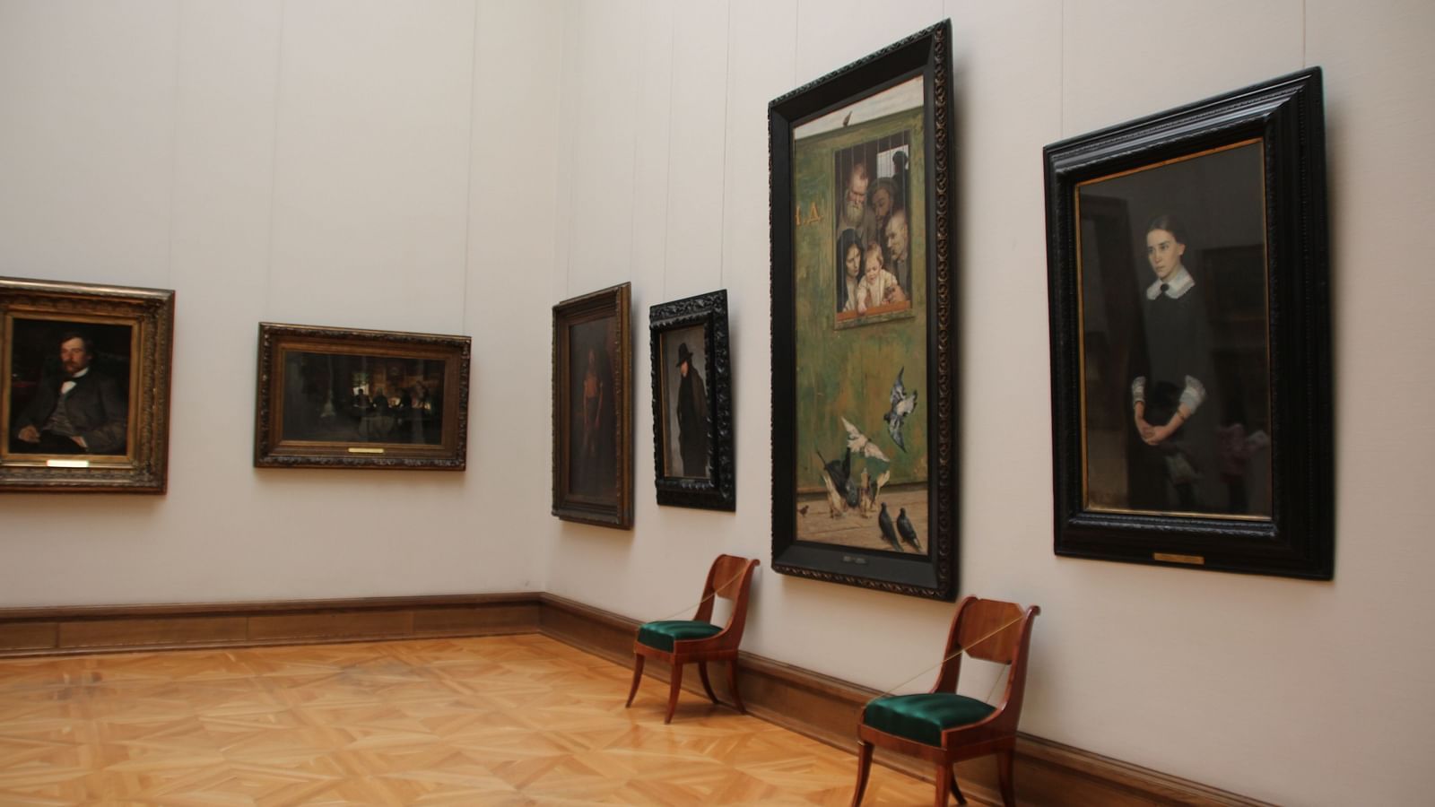 An overview of a museum with paintings hung on the wall and two chairs placed next to the wall.