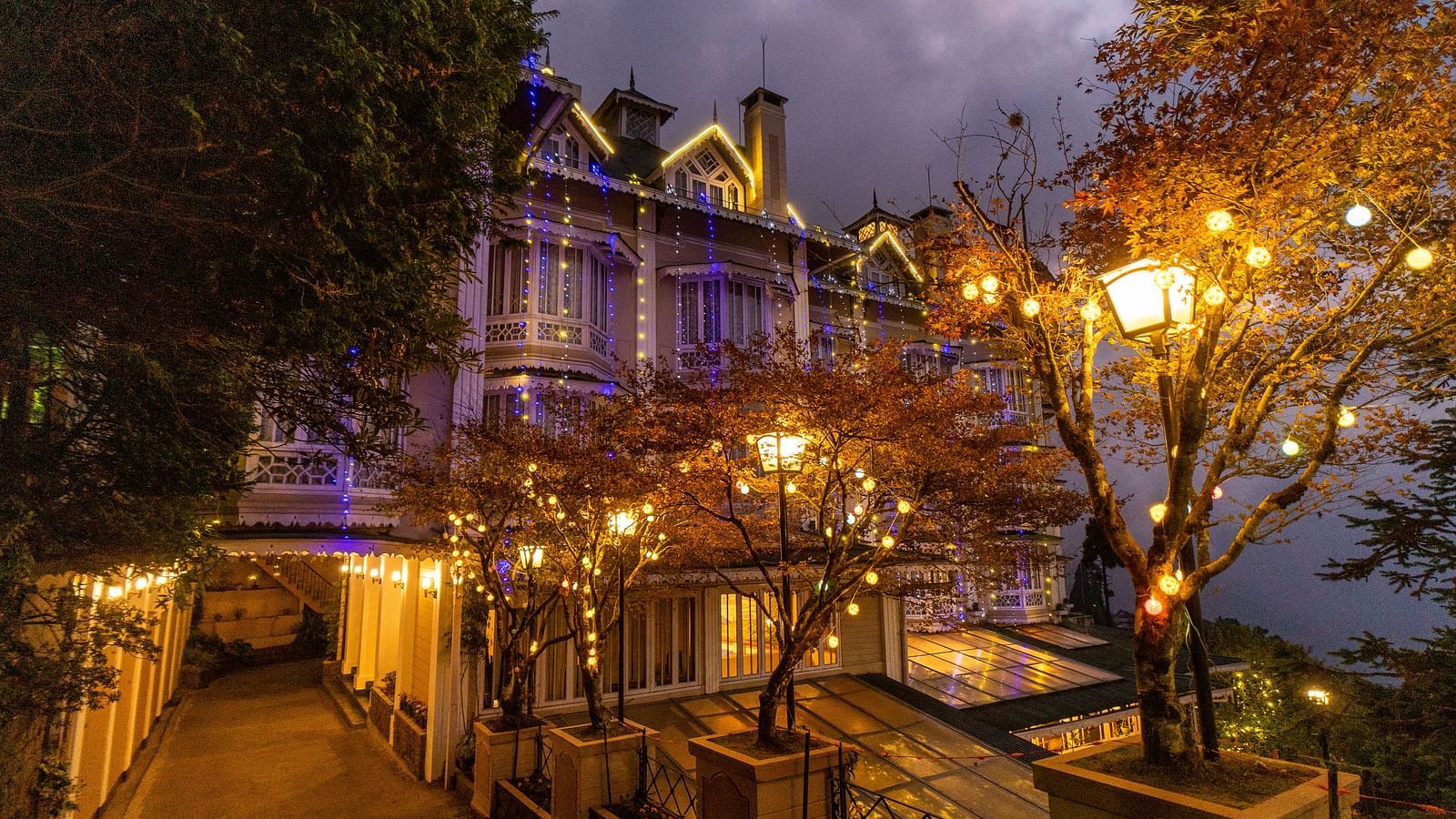 Cedar Inn, Darjeeling illuminated with warm evening lights, nestled amidst autumn trees and a peaceful walkway.
