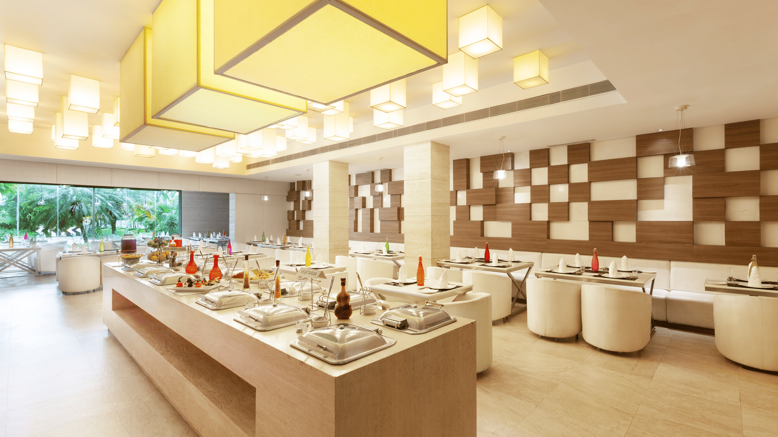 A diagonal view of a restaurant with an island in the middle featuring buffet items, surrounded by tables and chairs on the sides | Cenneys Gateway
