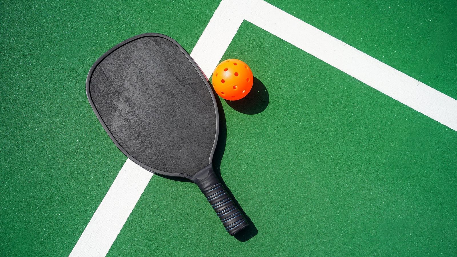 Image of a pickle ball and its racket kept on a green coloured court