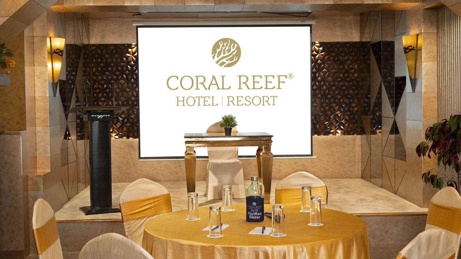 A banquet hall with decorated chairs and tables positioned to view the presentation screen on the dais