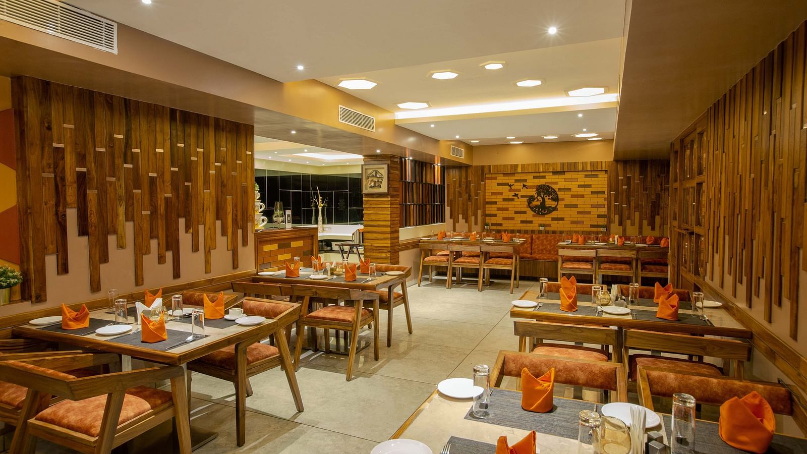 Image of Honeycomb Restaurant at Coral Reef Hotel & Spa in Port Blair showing dining setting of 4 chairs at each table and cutlery organised