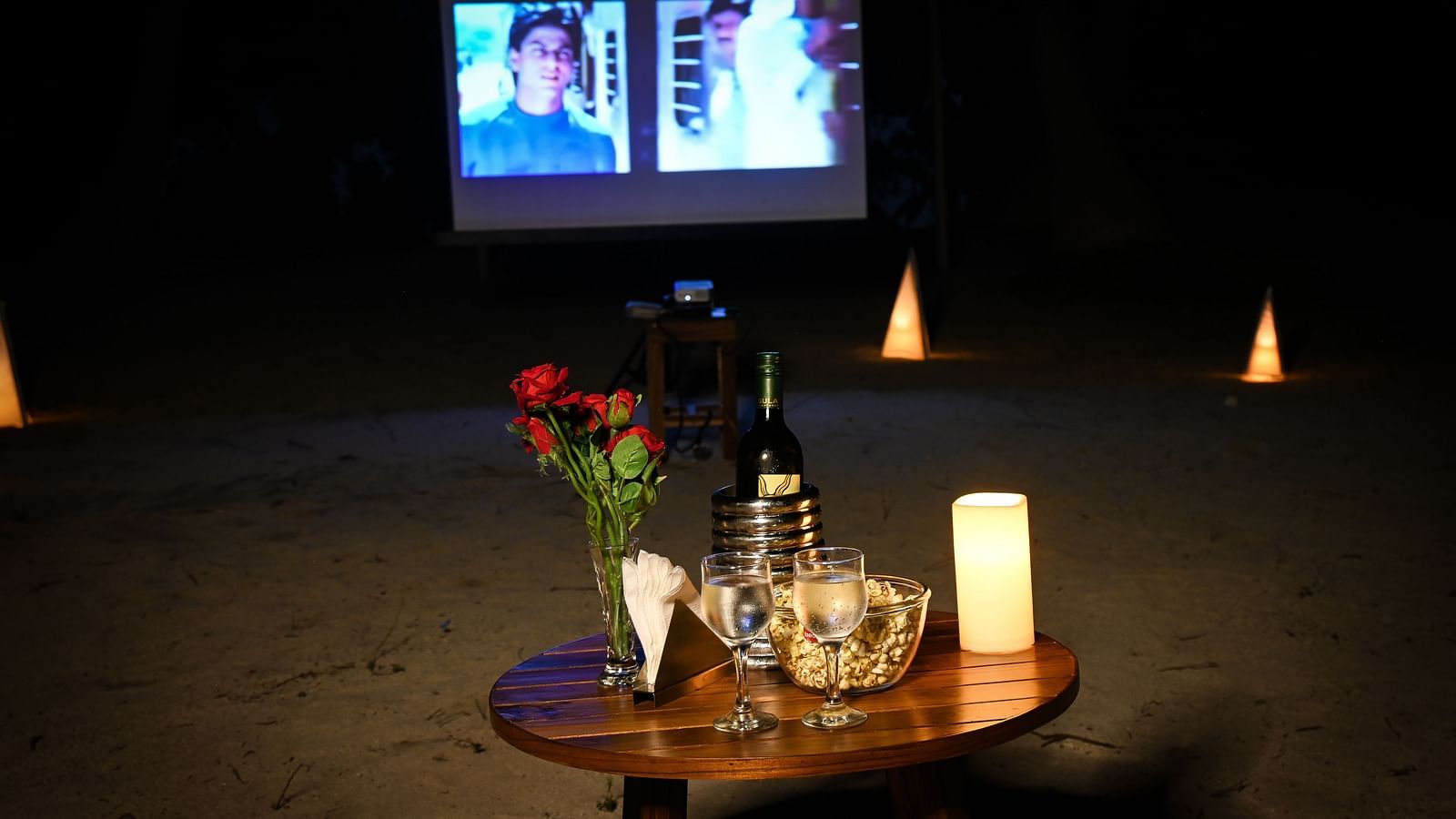A small table with glasses wine rose on top and a movie playing in the white screen in the background - Coral Reef Resort & Spa, Havelock