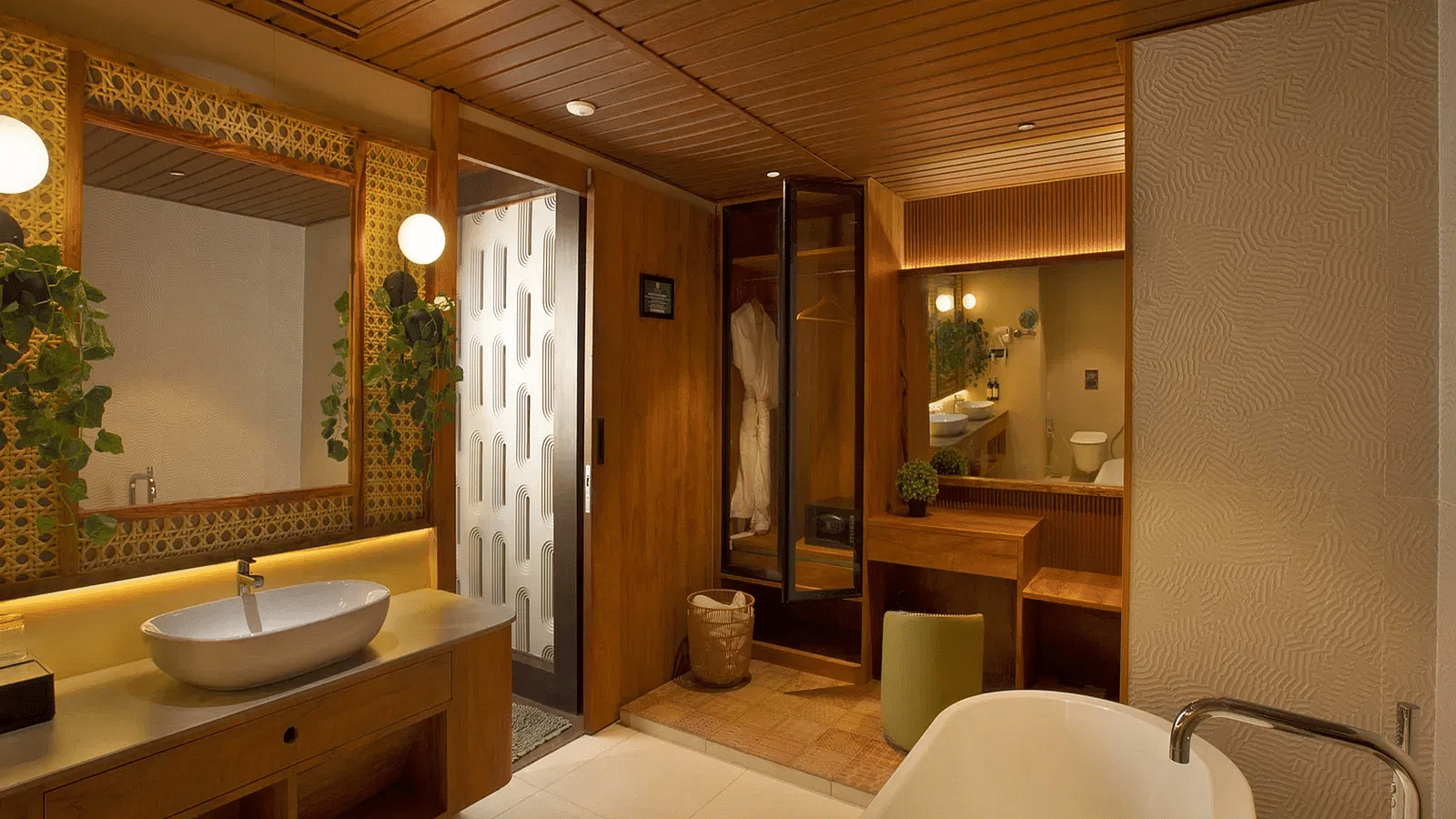 Bathroom of Coral Teal Suite at Coral Reef Resort and Spa in Havelock featuring a sink with a mirror over it and lamps on the both sides opposite to which is a bathroom and in another corner is a dressing mirror with a pouffe