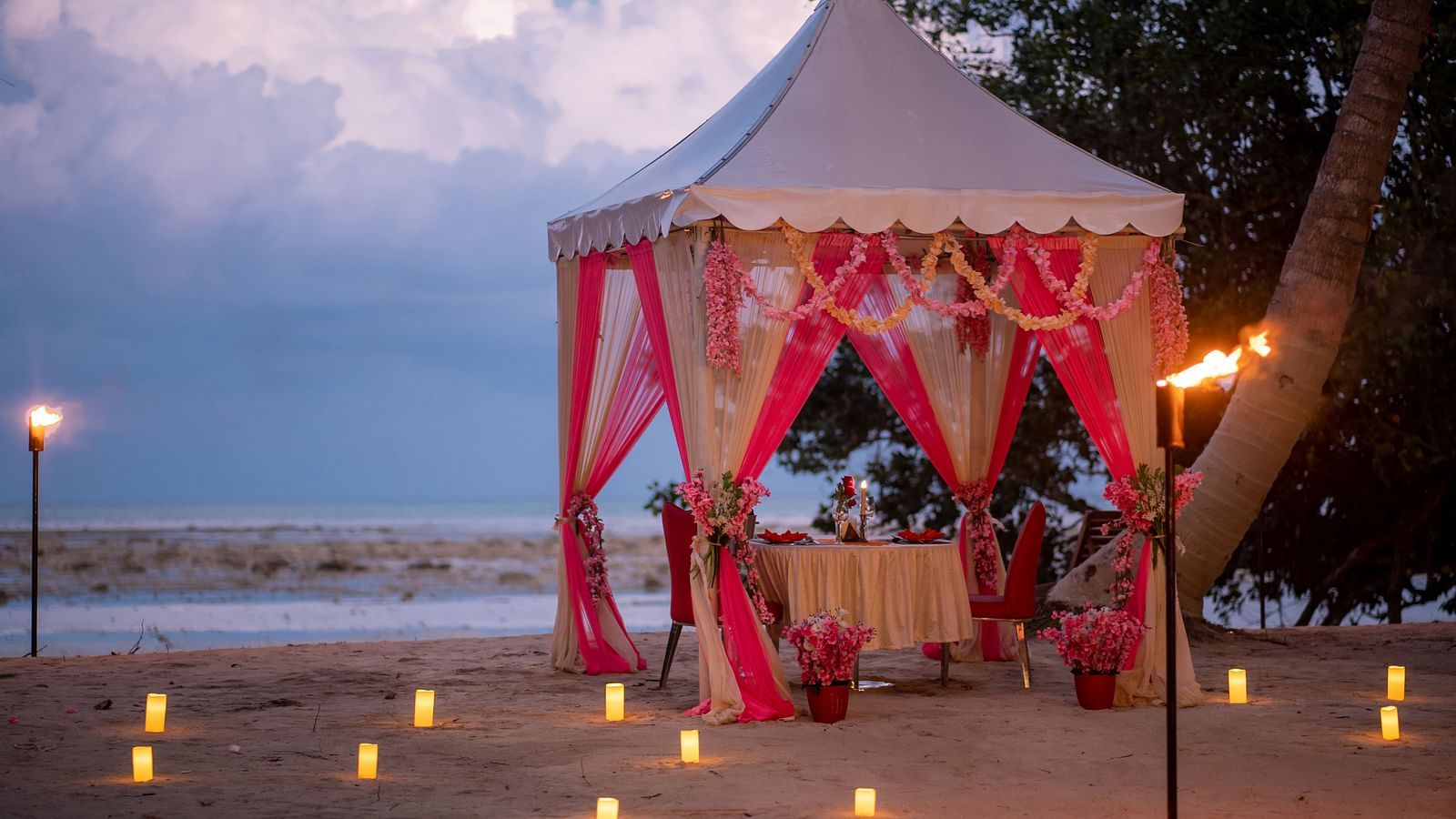 Romantic beachfront dining setup with a tent, candles and torches at dusk - Coral Reef Resort & Spa, Havelock