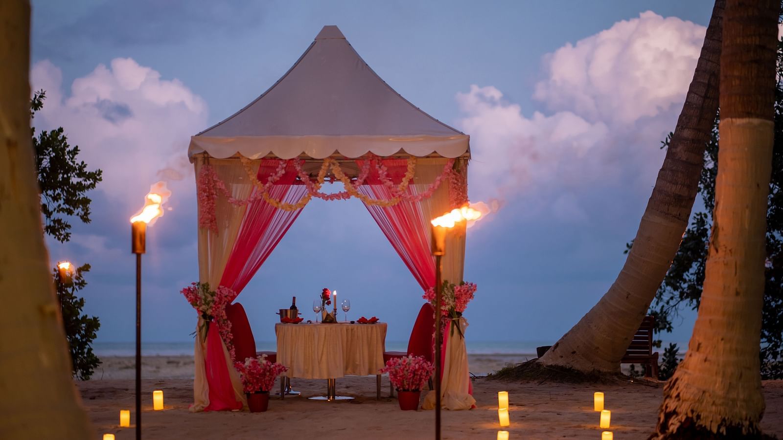 Elegant beach dining tent adorned with flowers and lit by torches in the evening twilight - Coral Reef Resort & Spa, Havelock