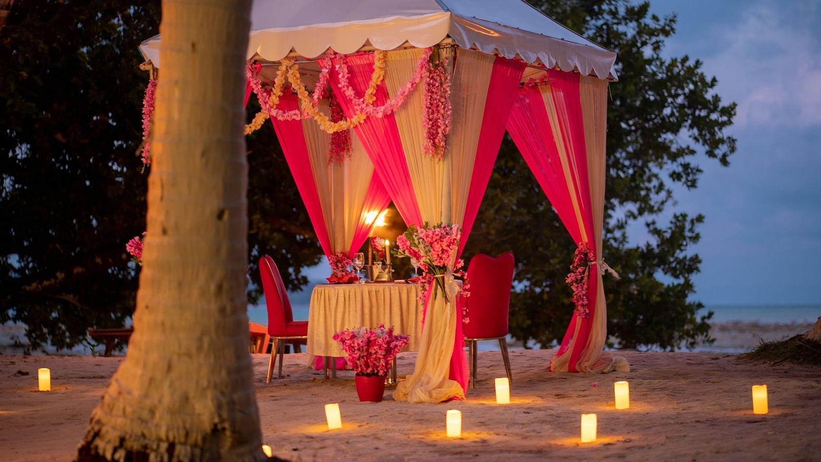 Intimate dining setting on a beach with a candle-lit table and a festively decorated tent - Coral Reef Resort & Spa, Havelock