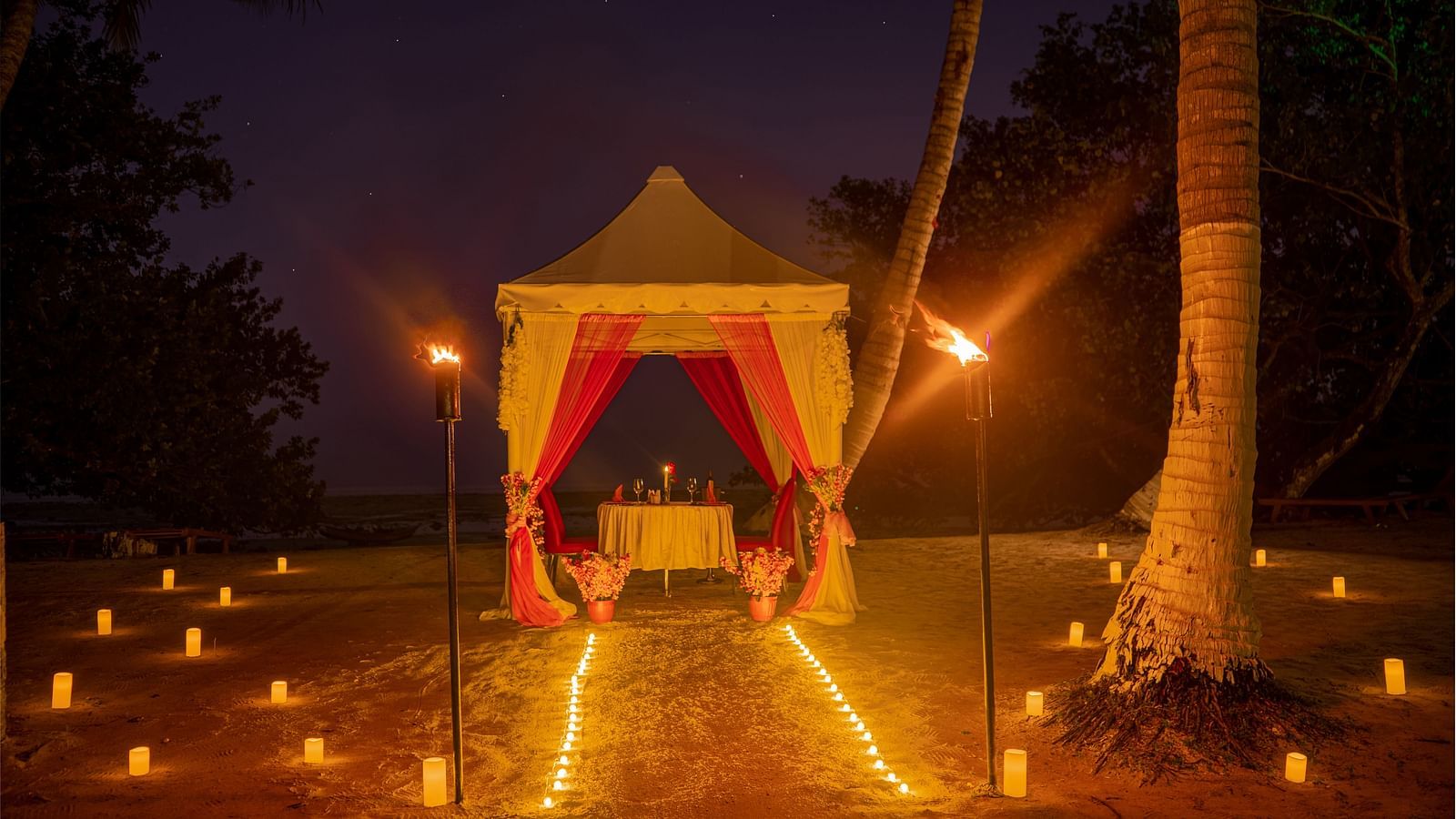A canopy set up on a beach at night with a path of candles leading to it and torches on either side - Coral Reef Resort & Spa, Havelock