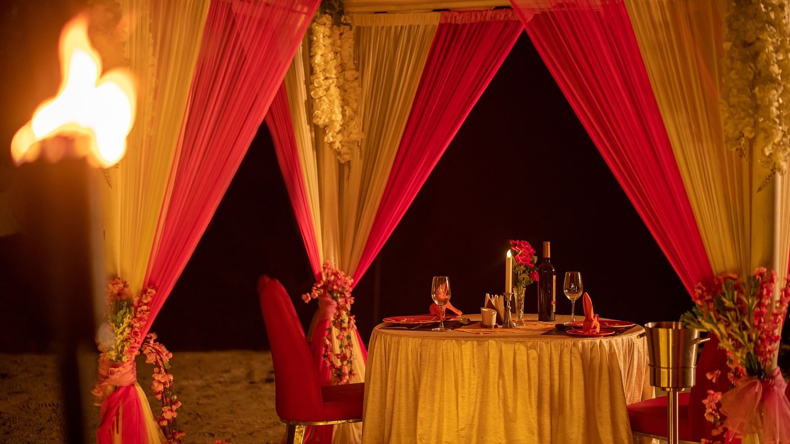 Inside view of a beach canopy with a dining table, lit by torches and surrounded by candles - Coral Reef Resort & Spa, Havelock