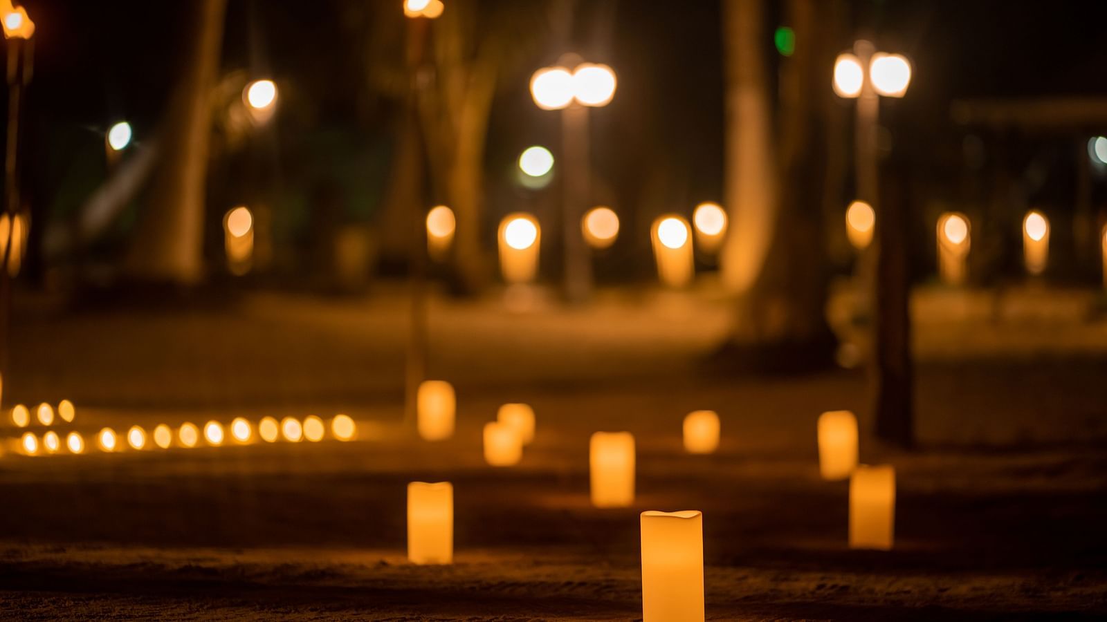 Illuminated candles on sand create a path at night with blurry lights in the background - Coral Reef Resort & Spa, Havelock