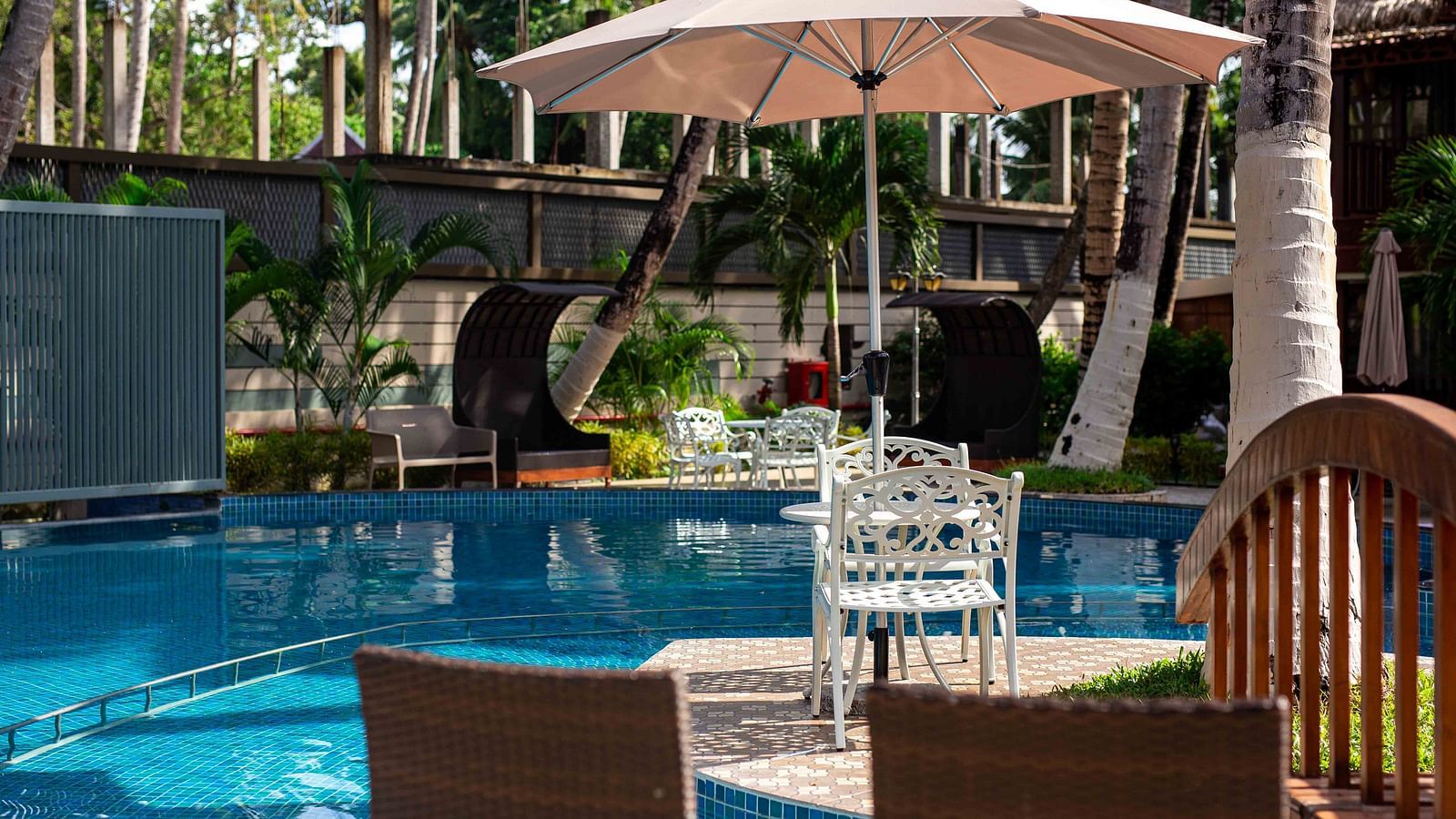 A pool area surrounded by tropical palm trees, with comfortable seating and a parasol at Splash Pool Bar. The tranquil setting offers a perfect space for relaxation - Coral Reef Resort & Spa, Havelock