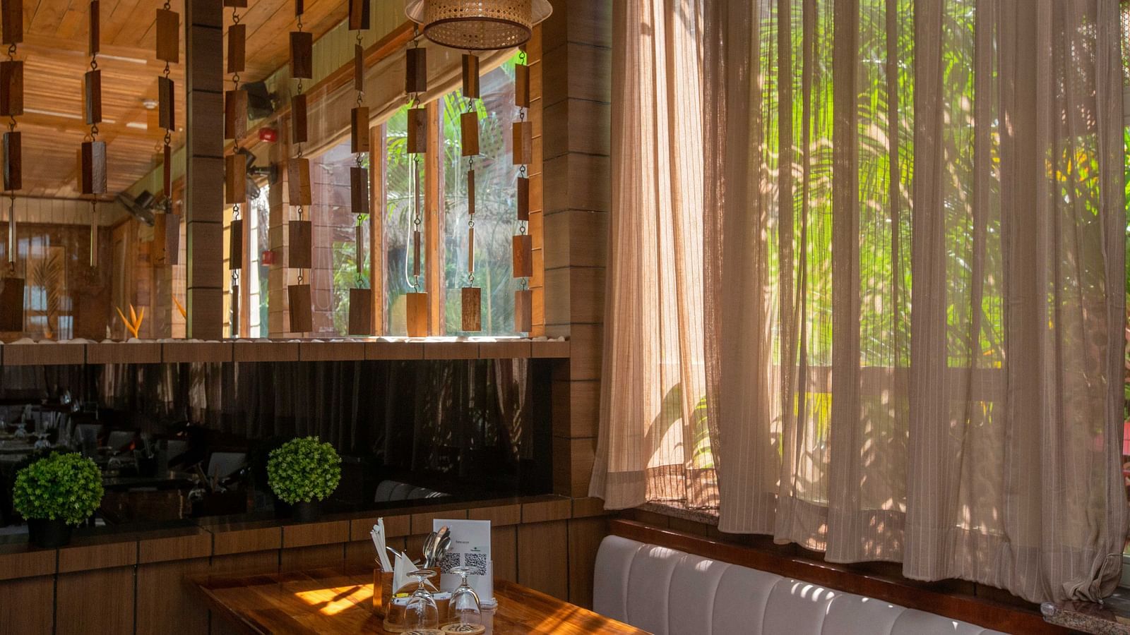 5th Bistro Cafe and Bar at Coral Reef Resort & Spa, Havelock featuring a stylish and modern area with sheer curtains letting in natural light. The space is lush with tropical plants, creating a relaxed yet sophisticated vibe - Coral Reef Resort & Spa, Have