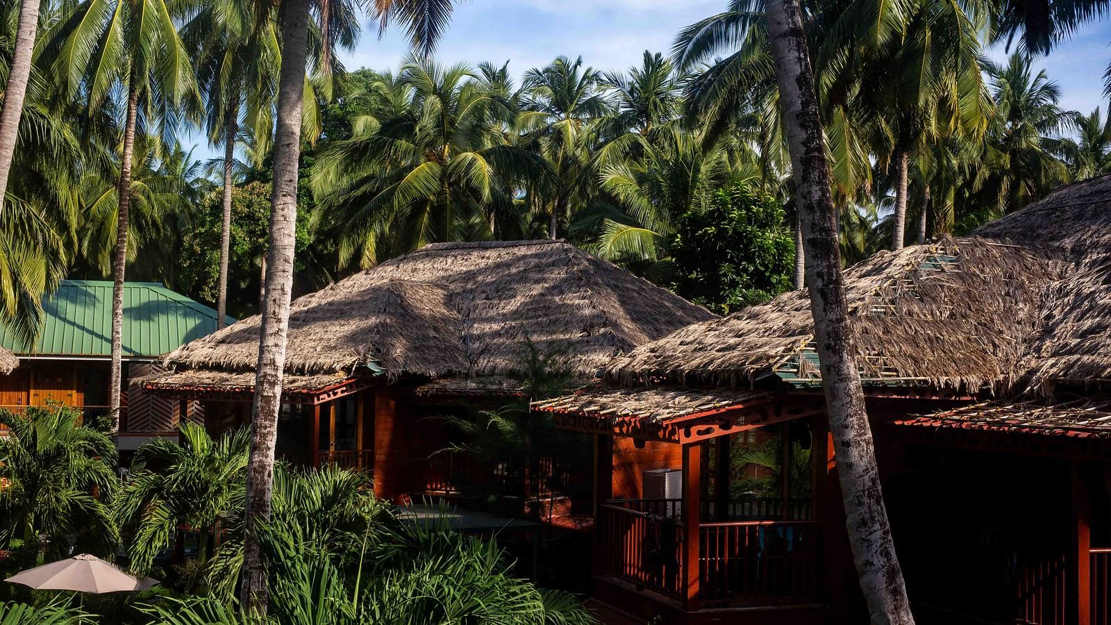 A cozy outdoor seating area with a thatched roof, surrounded by lush greenery. The space is perfect for relaxation, offering a calm and peaceful setting - Coral Reef Resort & Spa, Havelock