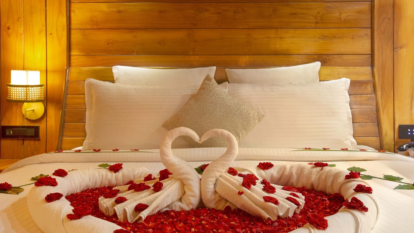  A close-up of a bed with romantic decorations, featuring heart-shaped towels and rose petals arranged in a heart design. The soft lighting enhances the intimate atmosphere - Coral Reef Resort & Spa, Havelock