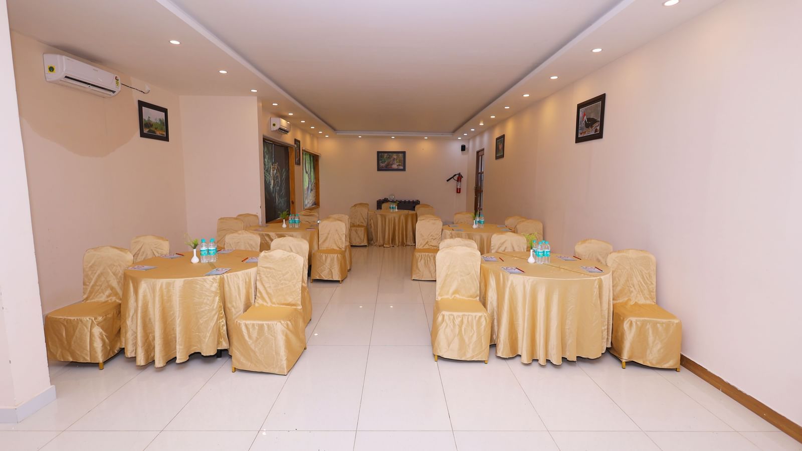 An empty banquet hall set up with tables and chairs draped in white and yellow linen at Corbett Nirvana Resort.