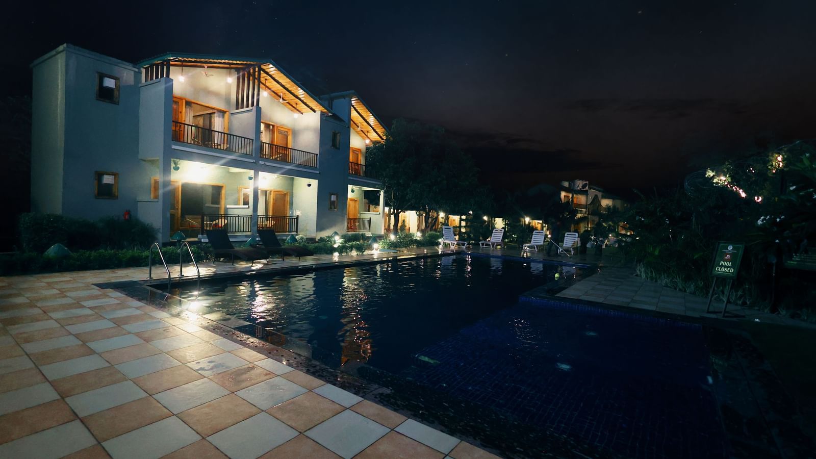 Side view of the swimming pool area with a bungalow in the side at Corbett Nirvana Resort during the night time.
