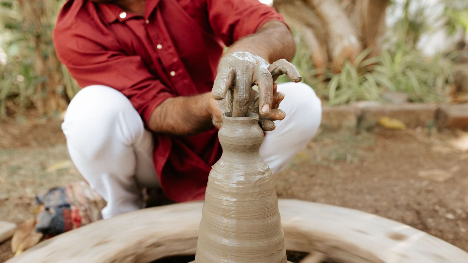 A person moulding clay on a pottery wheel placed outdoors at Daksh Eden Greenz, Sasan Gir.