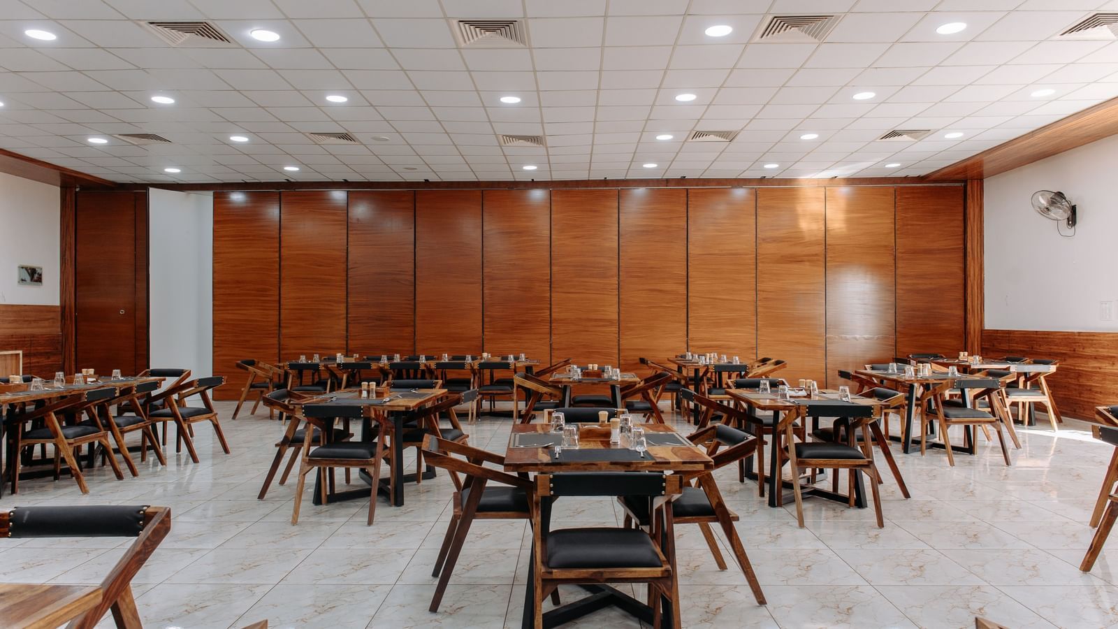  A wide angle shot of the restaurant at Daksh Eden Greenz in Sasan Gir, with various seating arrangements and overhead lighting.
