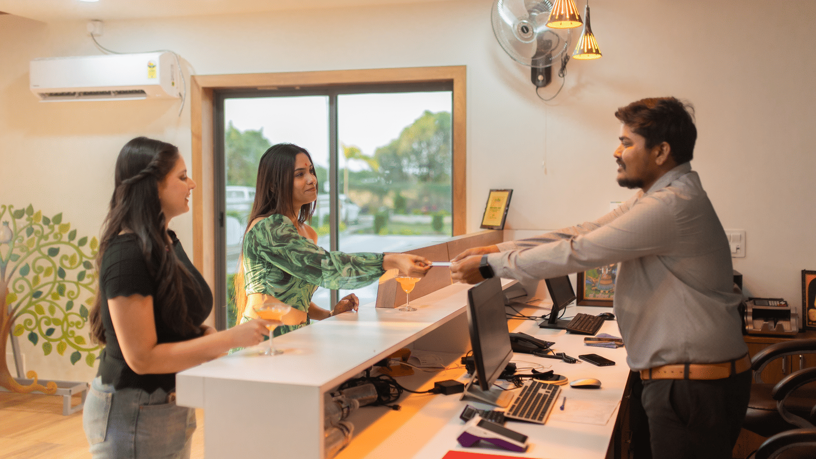 Three people speaking with eachother at the well-lit reception desk of Daksh Eden Greenz, Sasan Gir.