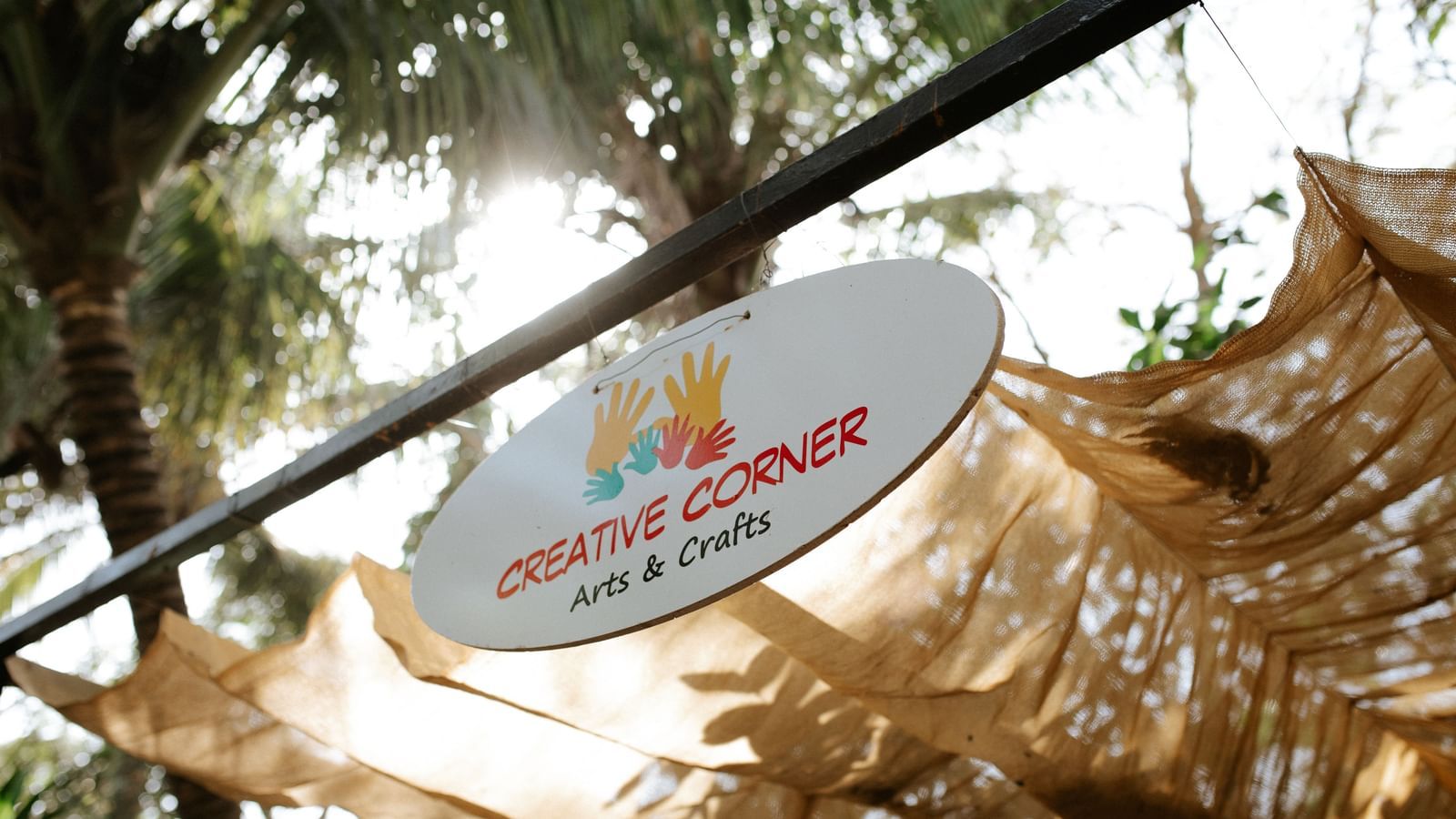 A sign board hung on a rod with the words 'creative corner' written on them and canopied by trees -Daksh Eden Greenz, Sasan Gir