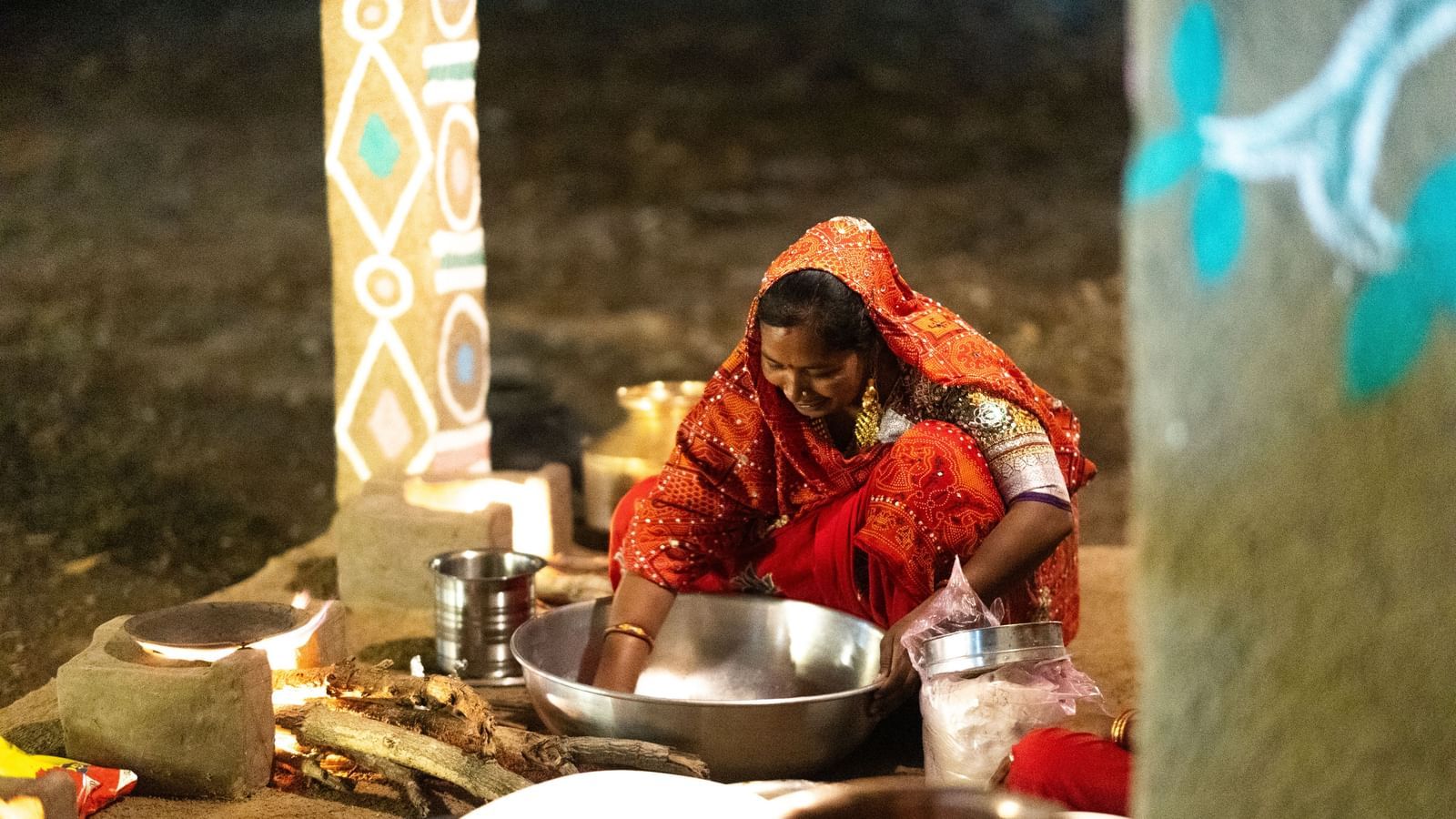 A woman preparing food in large steel utensils while seated on the ground in a traditionally built kitchen at Daksh Edden Greenz, Sasan Gir.