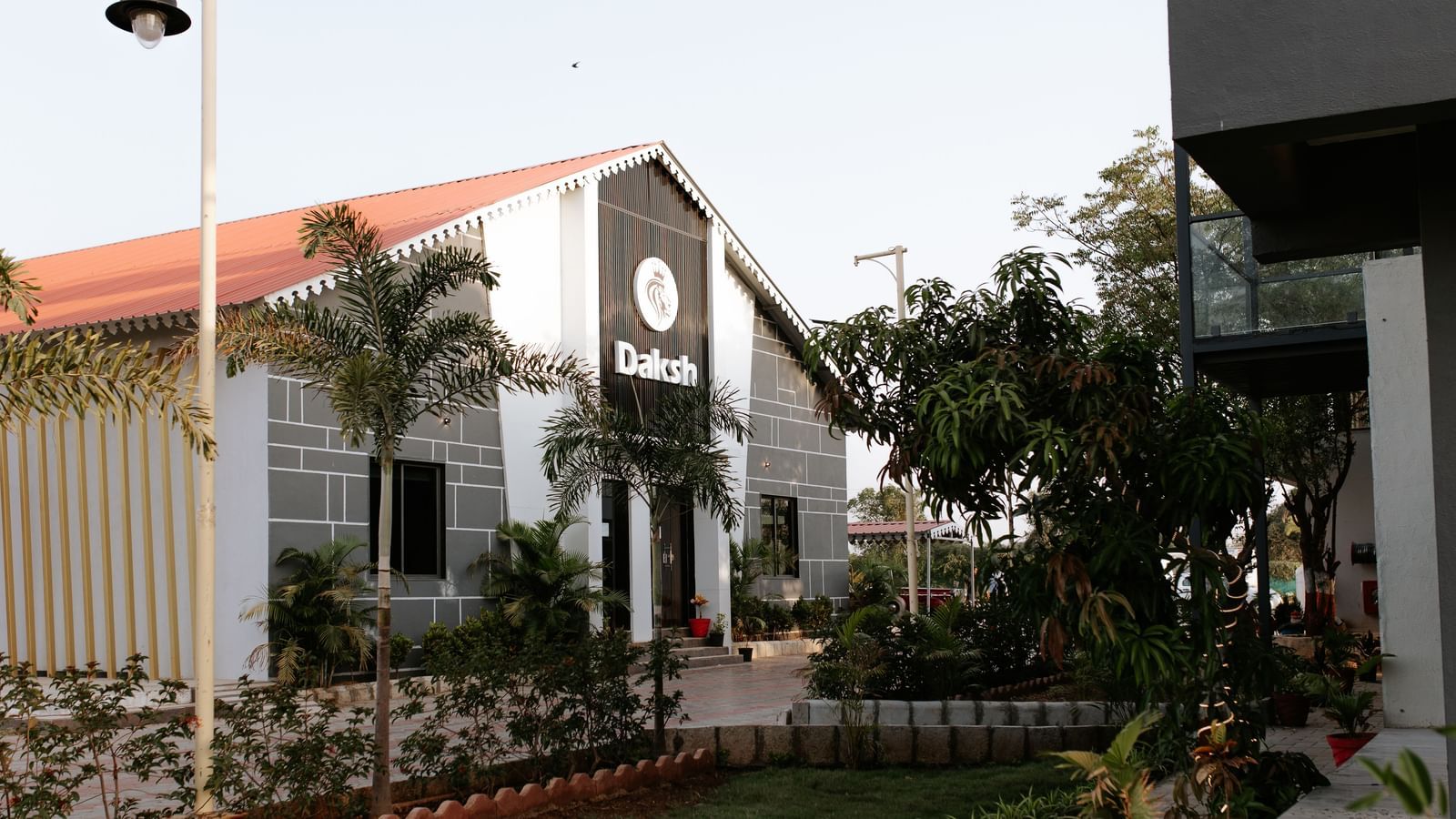 Garden view of Daksh Eden Greenz, Sasan Gir, featuring modern cottages surrounded by landscaped greenery and palm trees.