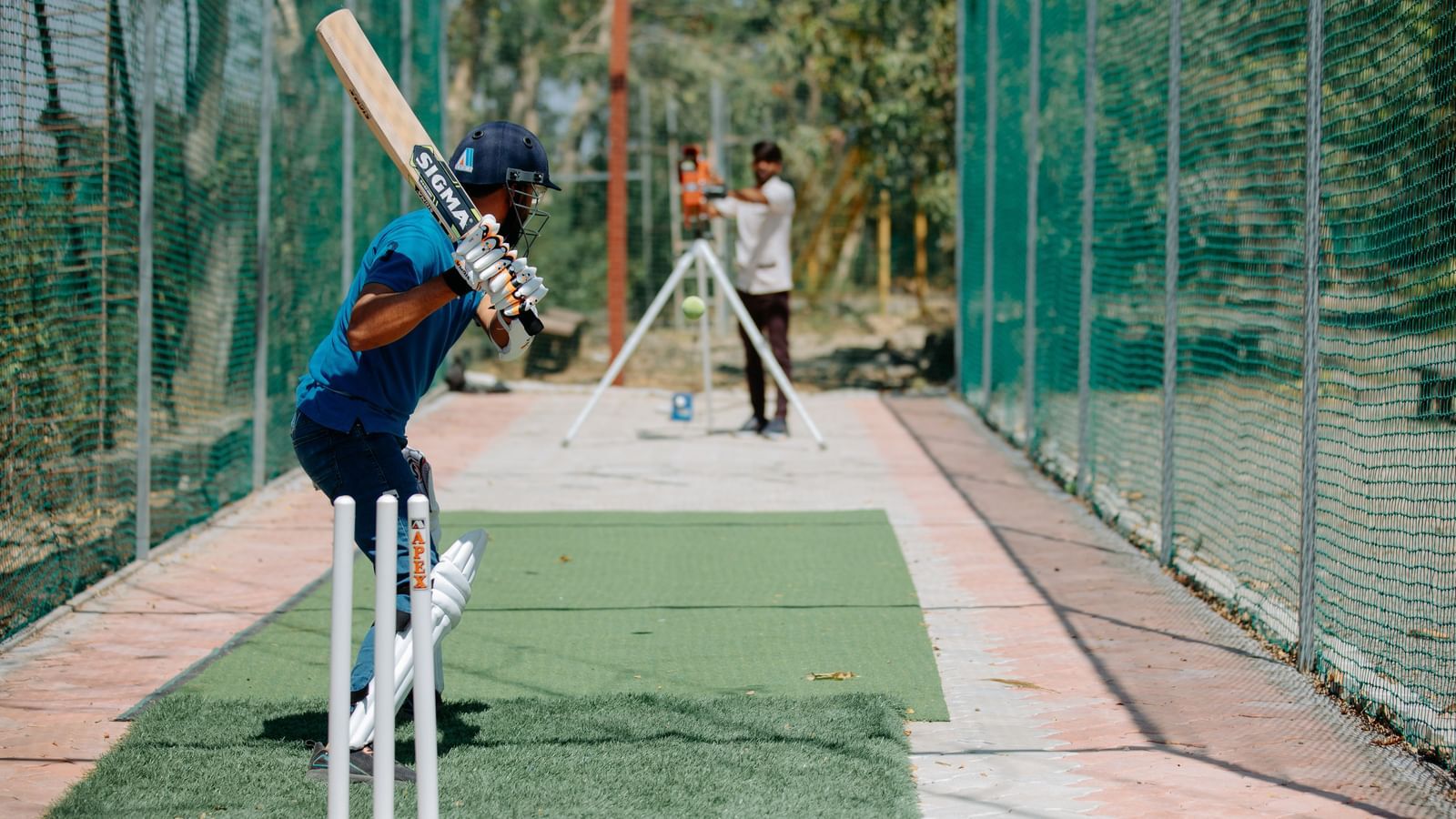 A person playing cricket in a practice net swinging a bat at Daksh Resort & Amusement Park.