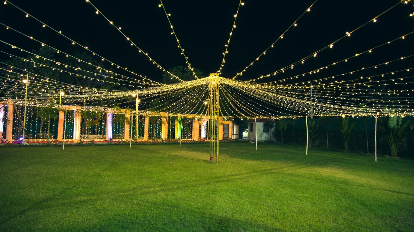 A wide view of lush lawn illuminated with hanging fairy lights arranged for an event at Daksh Resort and Amusement Park.