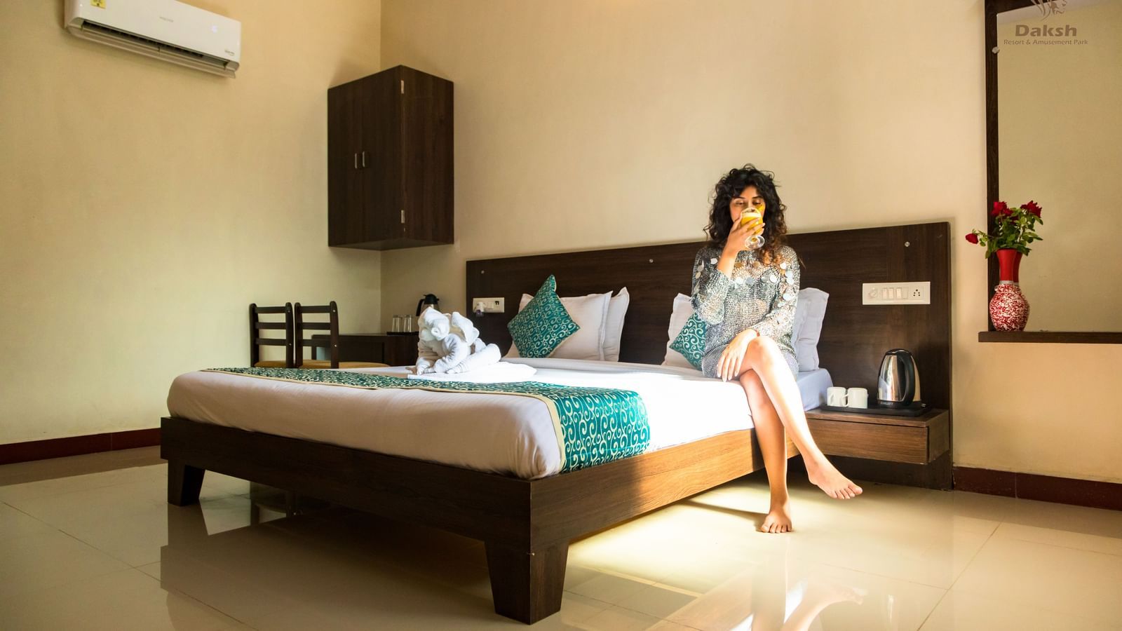A woman sitting on a bed in a guest room featuring wooden furnishings and an air-conditioning at Daksh Resort & Amusement Park.
