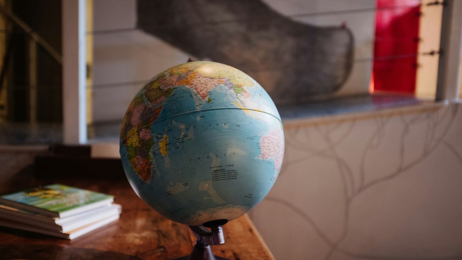 A globe kept on a table with books behind it.